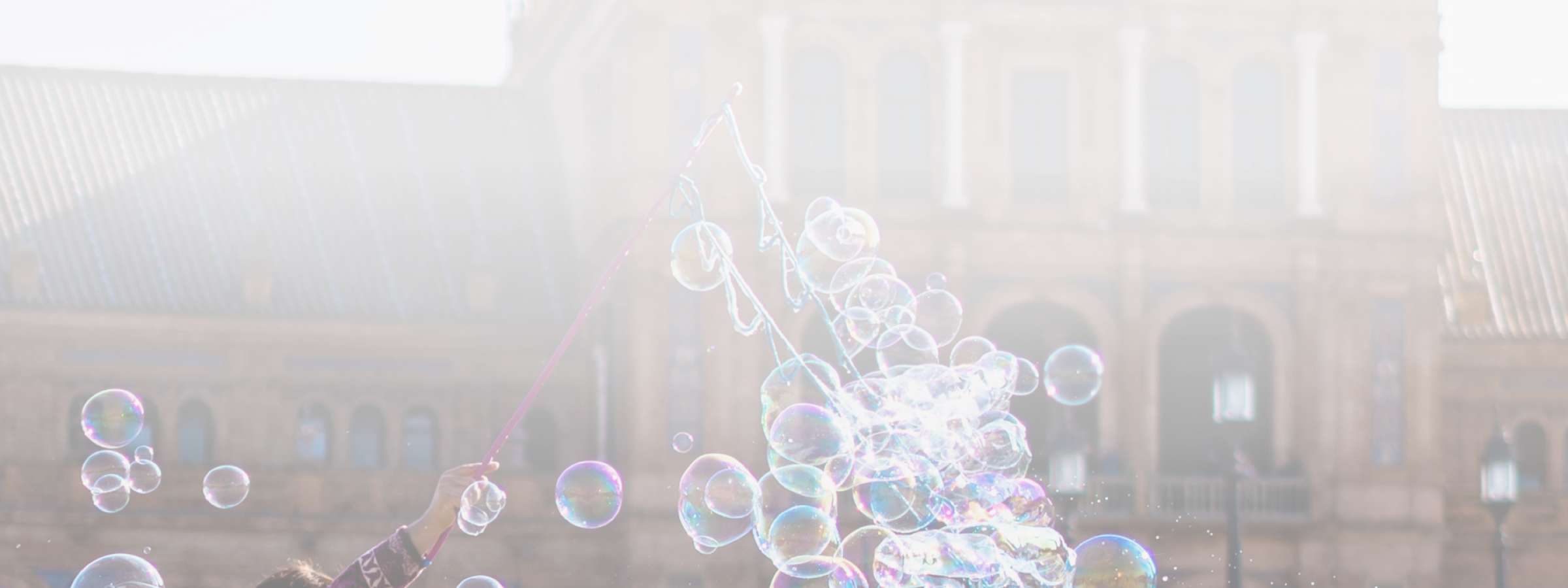 A man blows bubbles for a group of children in a city square